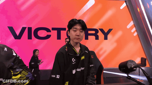 A Man Stands In Front Of A Large Victory Sign GIF