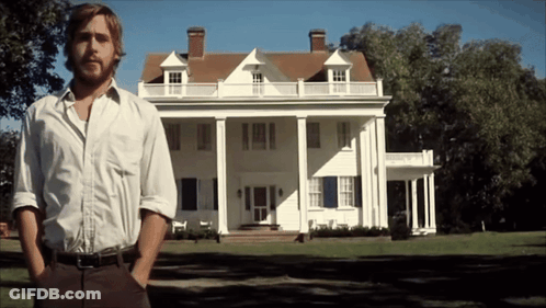 A Man Stands In Front Of A Large White House With His Hands In His Pockets GIF