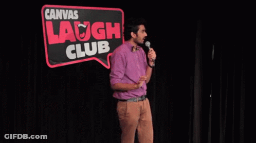 A Man Stands In Front Of A Microphone In Front Of A Sign That Says Canvas Laugh Club GIF