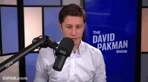 A Man Stands In Front Of A Microphone In Front Of A Sign That Says " The David Pakman Show " GIF