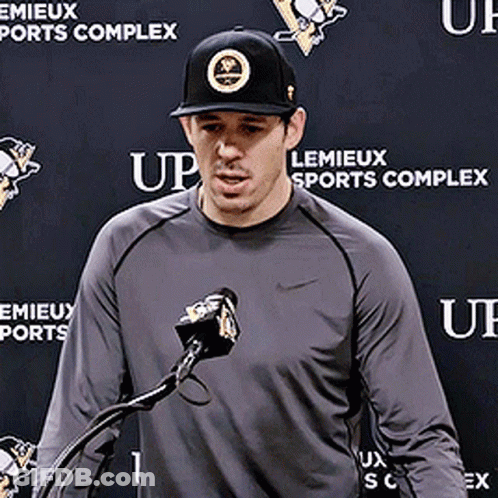 A Man Stands In Front Of A Microphone In Front Of A Wall That Says Lemieux Sports Complex GIF