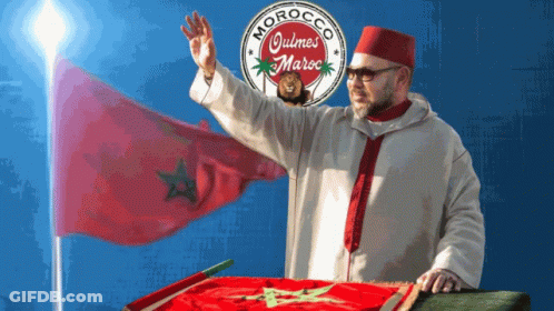 A Man Stands In Front Of A Morocco Quimes Maroc Logo GIF