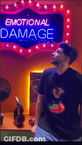 A Man Stands In Front Of A Neon Sign That Says Emotional Damage GIF