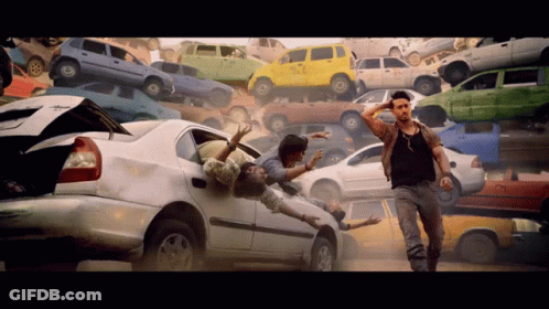 A Man Stands In Front Of A Pile Of Cars Including One That Has The Word Taxi On It GIF