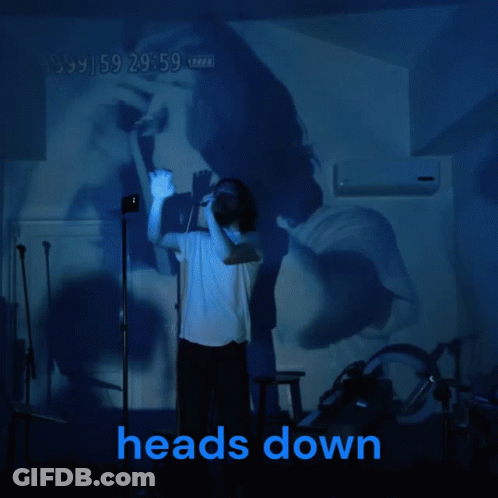 A Man Stands In Front Of A Projection Of A Woman And The Words Heads Down GIF