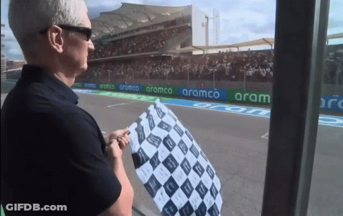 A Man Stands In Front Of A Race Track With Aramco Banners GIF
