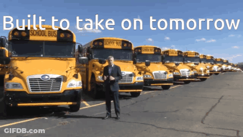A Man Stands In Front Of A Row Of School Buses With The Words Built To Take On Tomorrow Above Him GIF