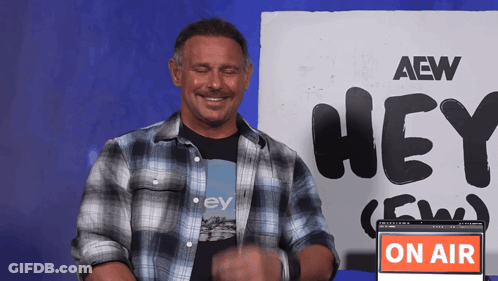 A Man Stands In Front Of A Sign That Says Aew Hey GIF