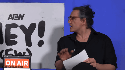 A Man Stands In Front Of A Sign That Says Aew On It GIF