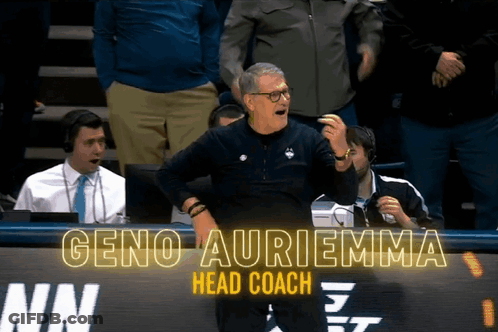 A Man Stands In Front Of A Sign That Says Geno Auriemma GIF
