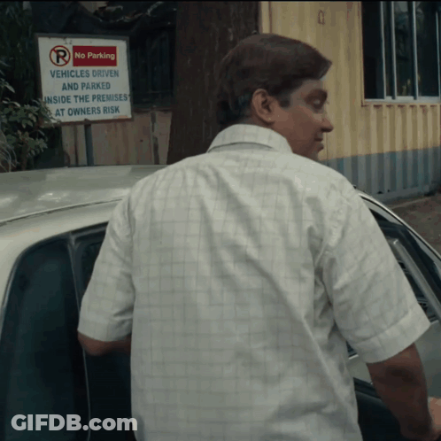 A Man Stands In Front Of A Sign That Says No Parking Vehicles Driven And Parked Inside The Premises At Owners Risk GIF