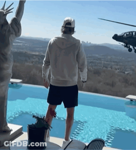 A Man Stands In Front Of A Statue Of Liberty And A Helicopter Flying Overhead GIF