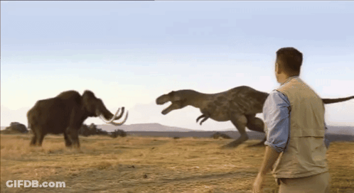 A Man Stands In Front Of A T-Rex And A Mammoth In A Field GIF