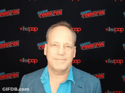 A Man Stands In Front Of A Wall That Says Comic Con On It GIF