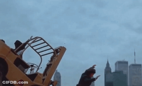 A Man Stands In Front Of A Yellow Forklift In A City GIF