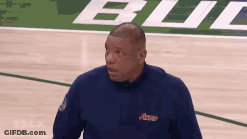 A Man Stands On A Basketball Court Wearing A Blue Shirt That Says Axerv GIF