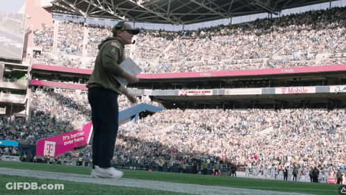 A Man Stands On A Football Field In Front Of A Sign That Says T Mobile GIF