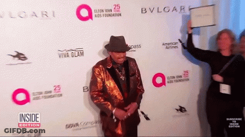 A Man Stands On A Red Carpet In Front Of A Wall That Says Bvlgari GIF