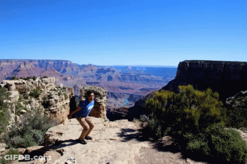 A Man Stands On A Rocky Cliff Overlooking A Canyon GIF