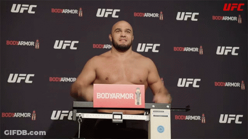 A Man Stands On A Scale In Front Of A Wall That Says Ufc GIF