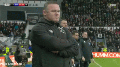 A Man Stands On A Soccer Field With His Arms Crossed In Front Of A Sky Sports Sign GIF