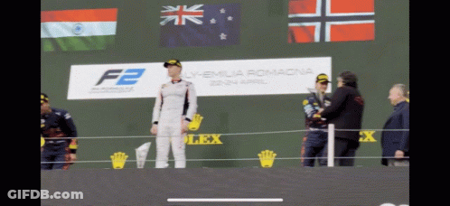 A Man Stands On A Stage In Front Of A Sign That Says F2 On It GIF