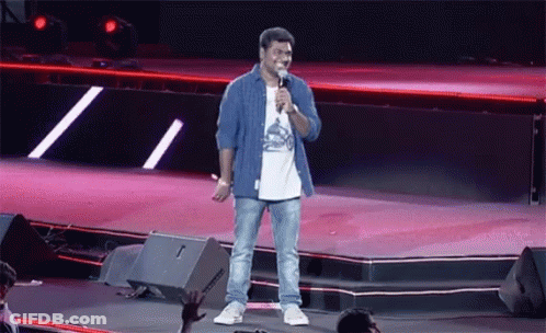 A Man Stands On A Stage With A Microphone In His Hand GIF