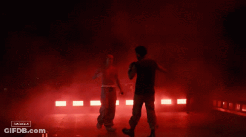 A Man Stands On A Stage With Red Lights Behind Him And The Words Cancella On The Bottom GIF