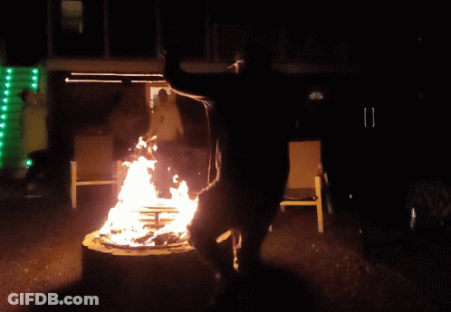 A Man Stands On A Stump In Front Of A Fire At Night GIF