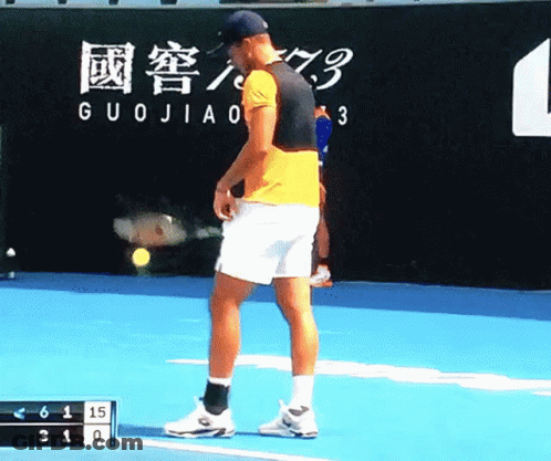 A Man Stands On A Tennis Court In Front Of A Wall That Says Guojiao On It GIF