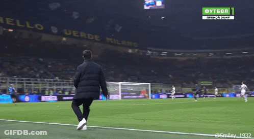 A Man Stands On The Edge Of A Soccer Field In Front Of A Banner That Says Anello Verde Milano GIF
