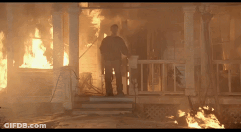 A Man Stands On The Porch Of A House That Is On Fire GIF