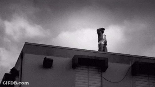 A Man Stands On The Roof Of A Building Looking Up At The Sky GIF