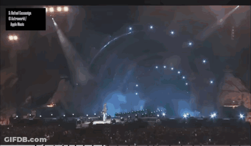 A Man Stands On Top Of A Stage With A Sign That Says Apple Music GIF