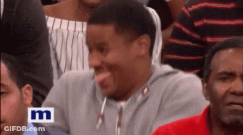 A Man Sticking His Tongue Out While Sitting In A Crowd With The Letter M On The Bottom Right GIF