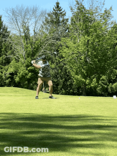 A Man Swings A Golf Club At A Golf Ball On A Golf Course GIF