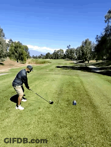 A Man Swings A Golf Club At A Golf Ball On A Golf Course GIF