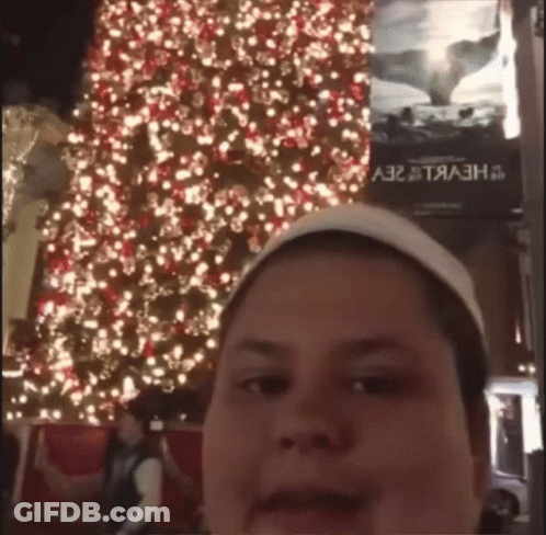 A Man Taking A Picture In Front Of A Christmas Tree GIF