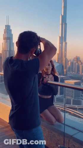 A Man Taking A Picture Of A Woman Sitting On A Balcony GIF