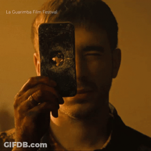 A Man Taking A Picture Of Himself With A La Guarimba Film Festival Advertisement In The Background GIF