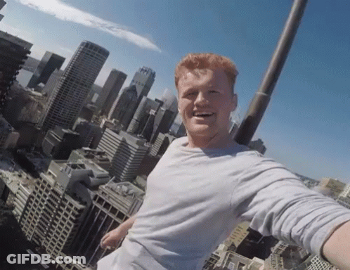 A Man Taking A Selfie On Top Of A Building With A City Skyline In The Background GIF