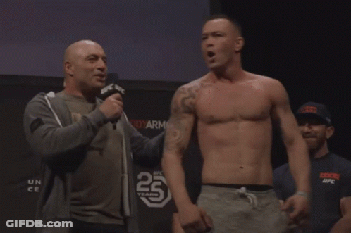 A Man Talking Into A Microphone In Front Of A Sign That Says 25 Years On It GIF