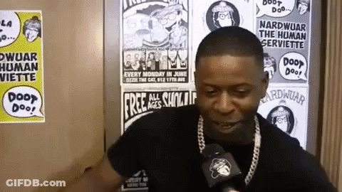 A Man Talking Into A Microphone In Front Of A Wall With Posters On It That Say Door Doo GIF