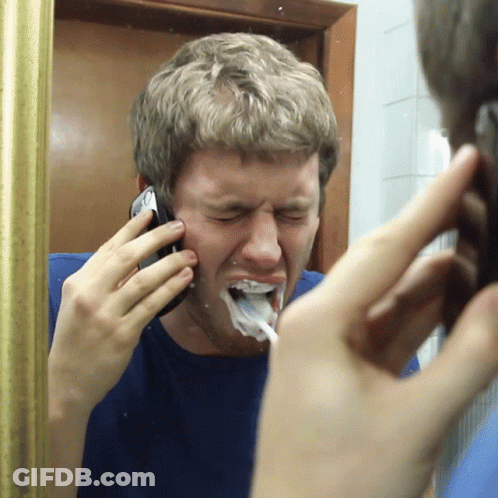 A Man Talking On A Cell Phone While Brushing His Teeth In Front Of A Mirror GIF