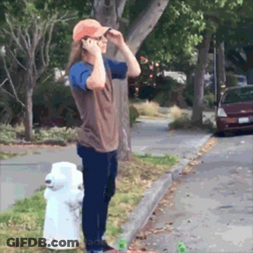 A Man Talking On A Cell Phone While Standing Next To A White Fire Hydrant GIF