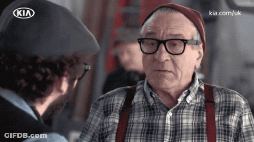 A Man Talking To An Older Man With Glasses And Suspenders And A Kia Logo On His Hat GIF