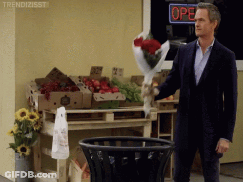 A Man Throws A Bouquet Of Roses Into A Trash Can In Front Of A Store That Is Open GIF