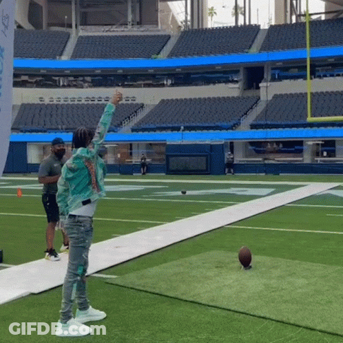 A Man Throws A Football On A Field With A Flag That Says Nfl GIF
