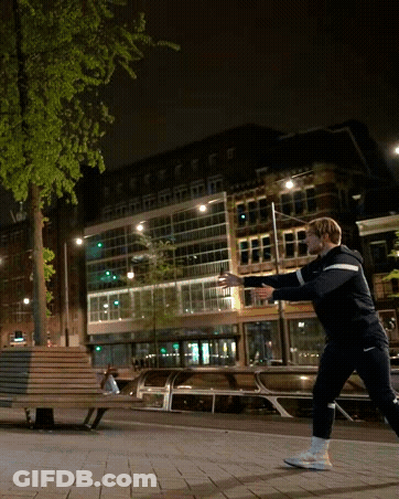A Man Throws A Frisbee In A City At Night GIF