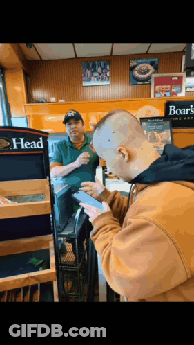 A Man Using A Cell Phone In Front Of A Sign That Says Boar 'S Head GIF